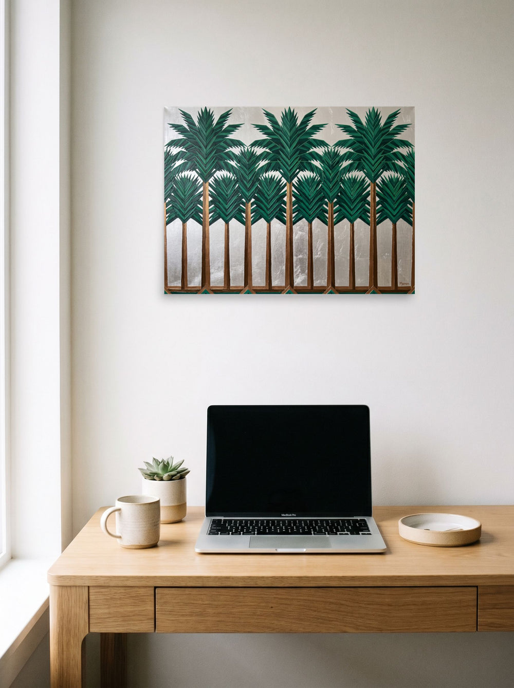 A 24x18 inch unframed paper Art Deco print of 'The Emerald Grove' hanging above a worktable with a laptop.
