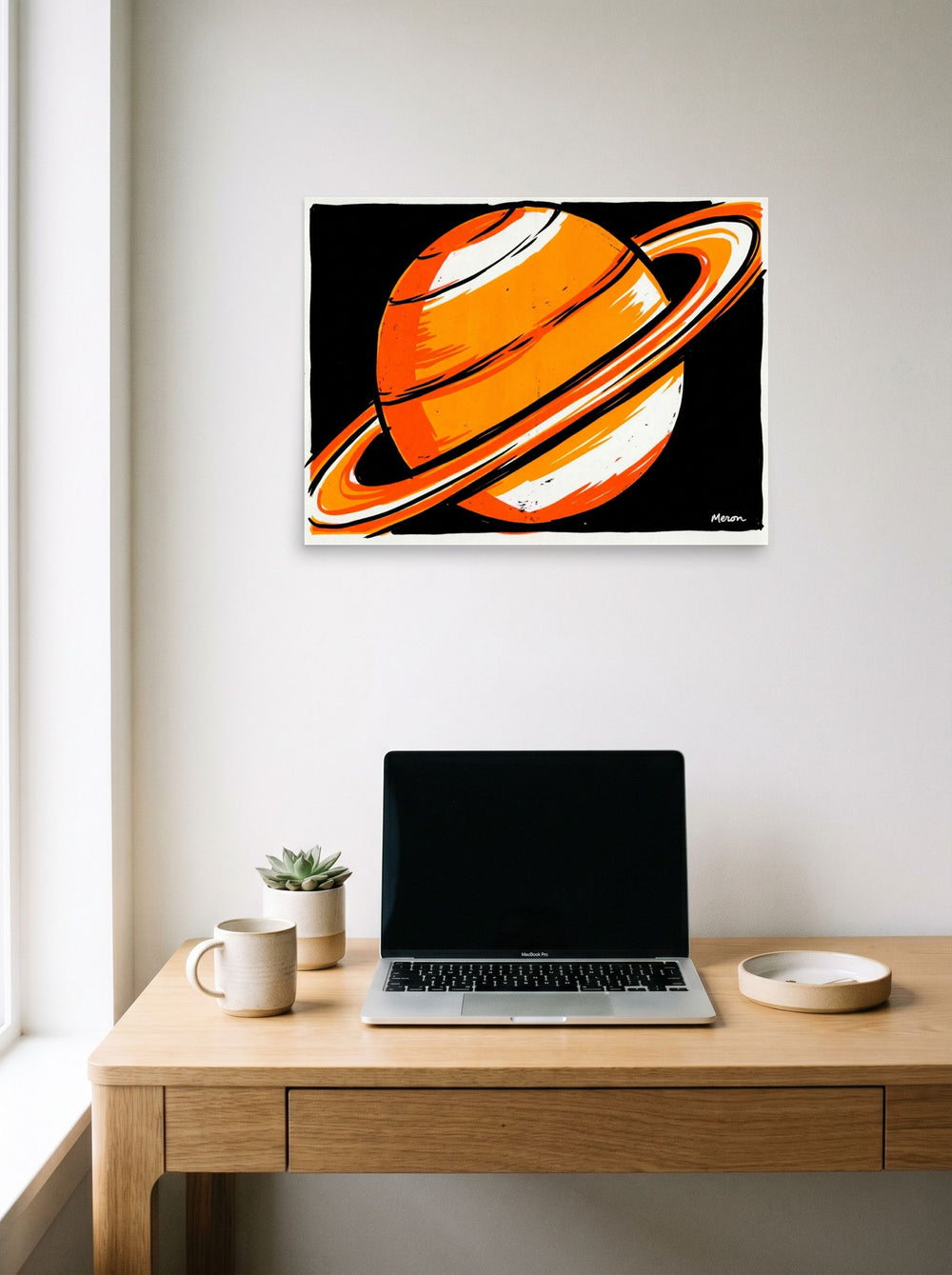 A 24x18 inch unframed paper Pop art print of 'Orange Orbit' hanging above a worktable with a laptop.