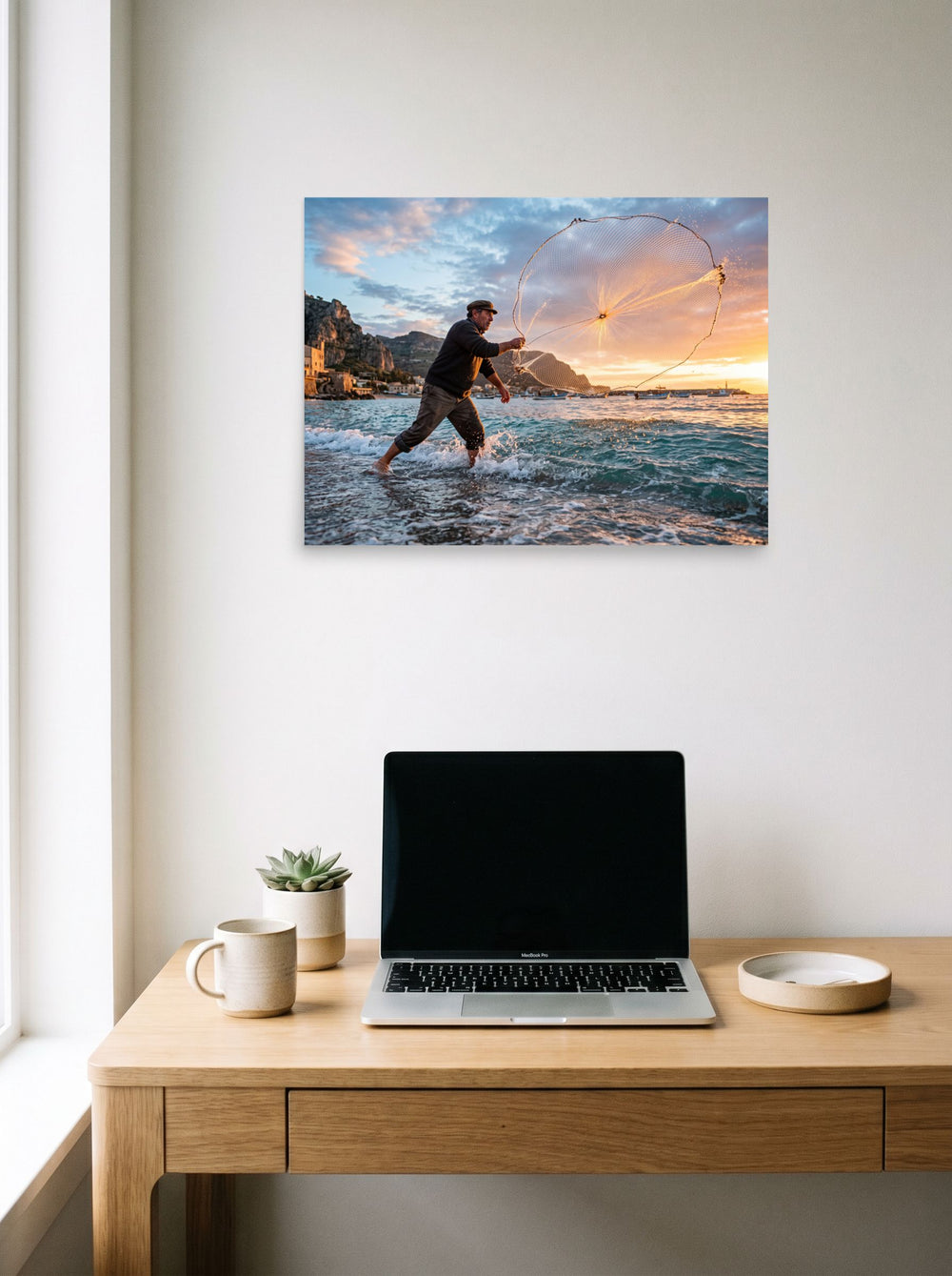 A 24x18 inch unframed paper Art photography print of 'Casting the Dawn' hanging above a worktable with a laptop.