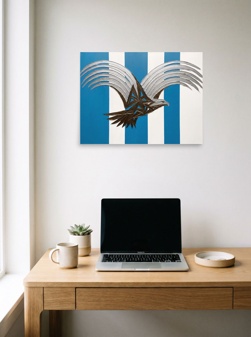 A 24x18 inch unframed paper Art Deco print of 'Deco Eagle in Flight' hanging above a worktable with a laptop.