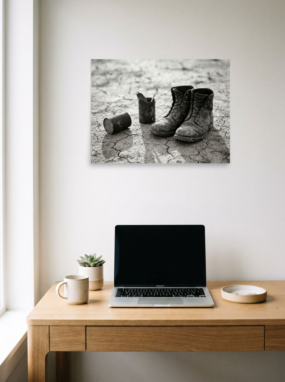 A 24x18 inch unframed paper American realism print of 'The Drifter's Boots' hanging above a worktable with a laptop.