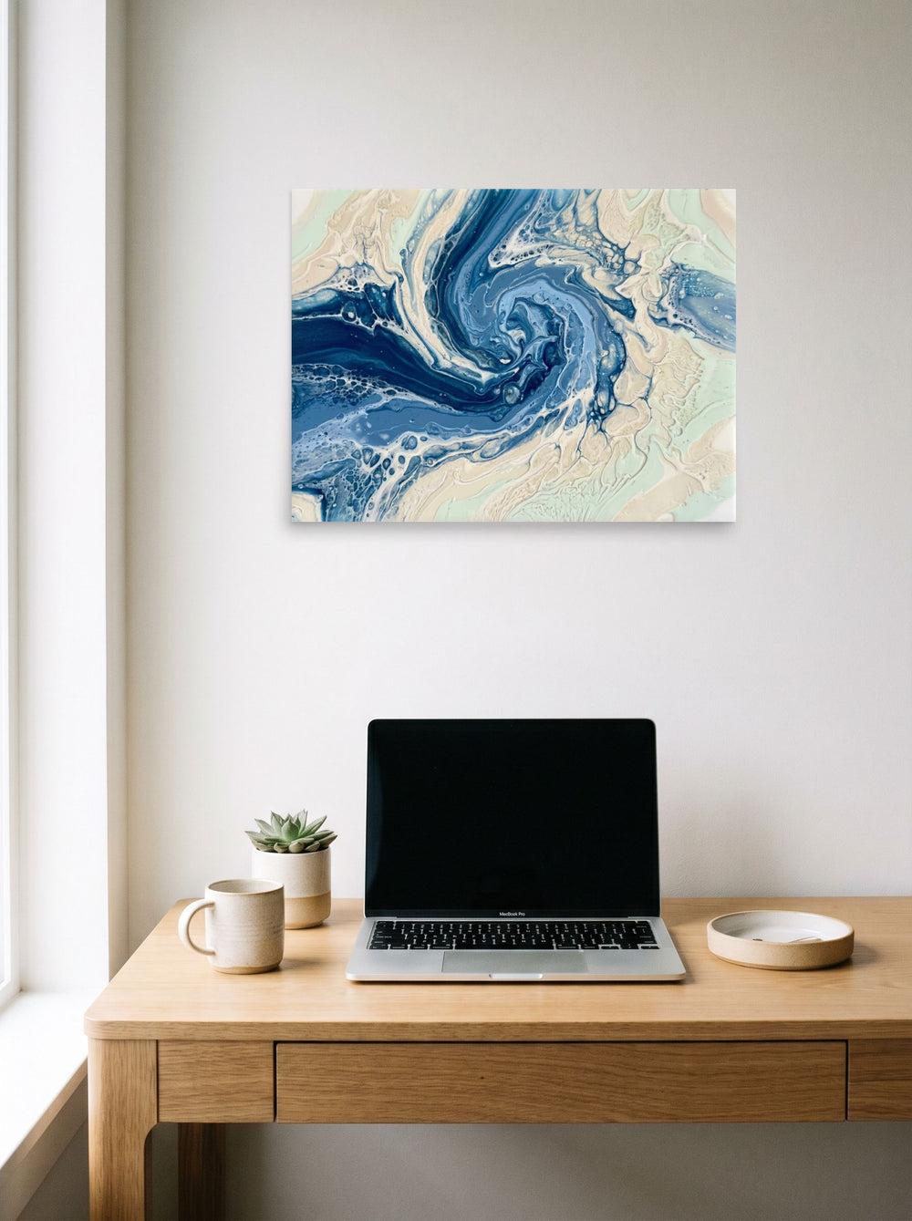 A 24x18 inch unframed paper Abstract art print of 'Ocean Whirlpool' hanging above a worktable with a laptop.