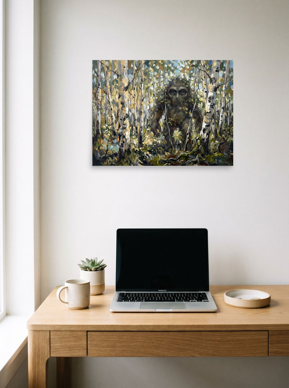 A 24x18 inch unframed paper Expressionism print of 'Forest Watcher' hanging above a worktable with a laptop.