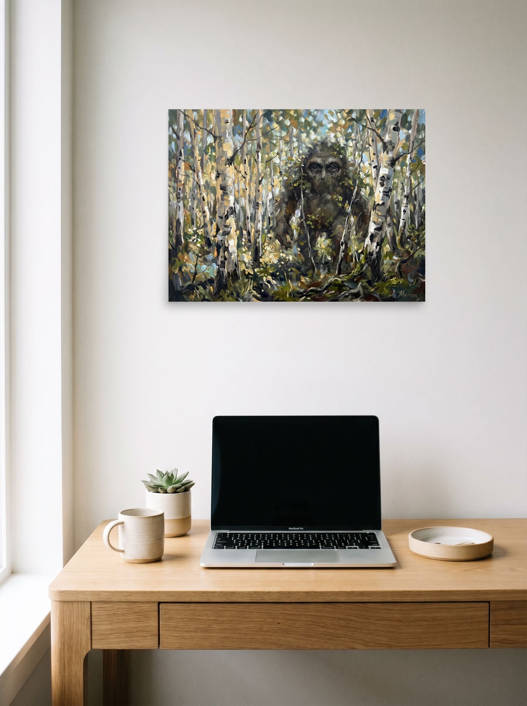 A 24x18 inch unframed paper Expressionism print of 'Forest Watcher' hanging above a worktable with a laptop.