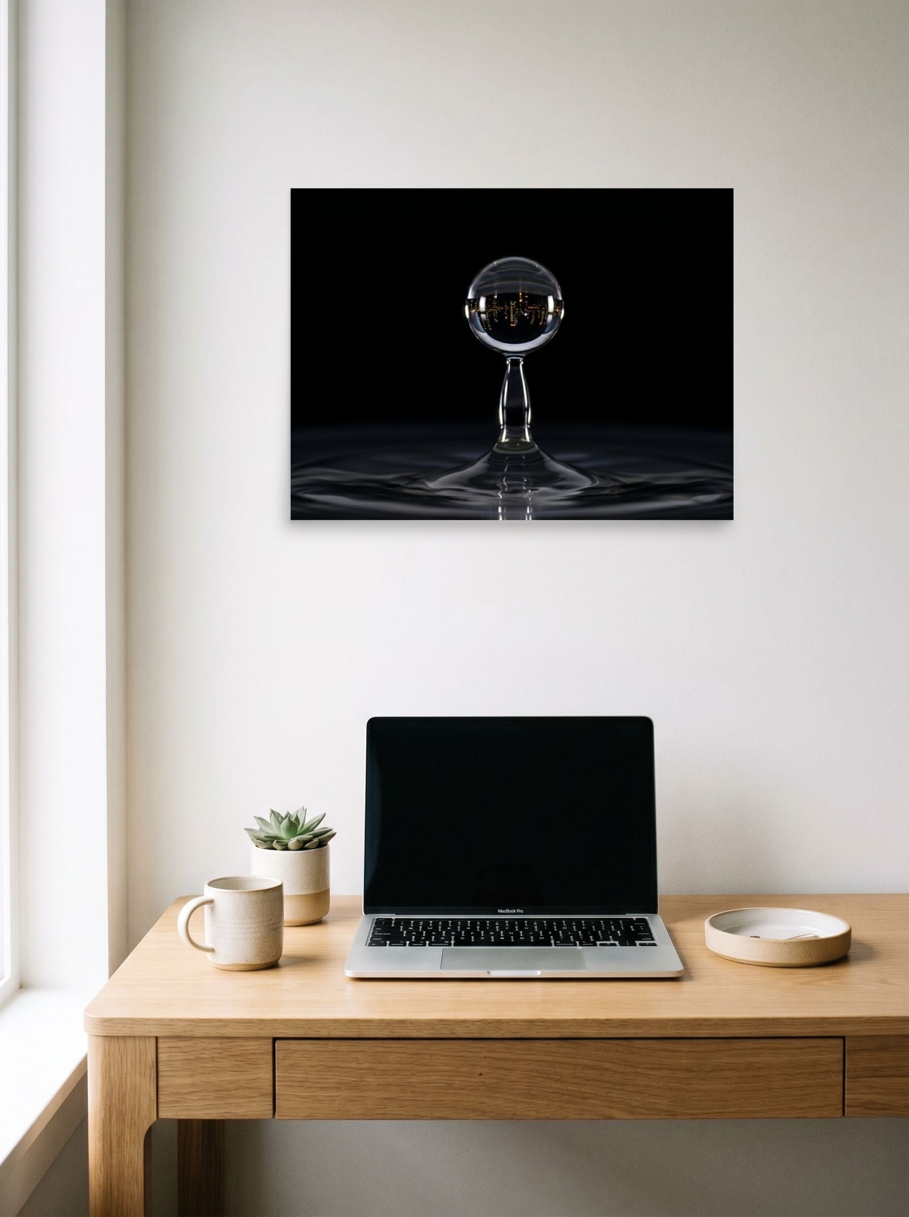 A 24x18 inch unframed paper Surrealism print of 'City in a Drop' hanging above a worktable with a laptop.