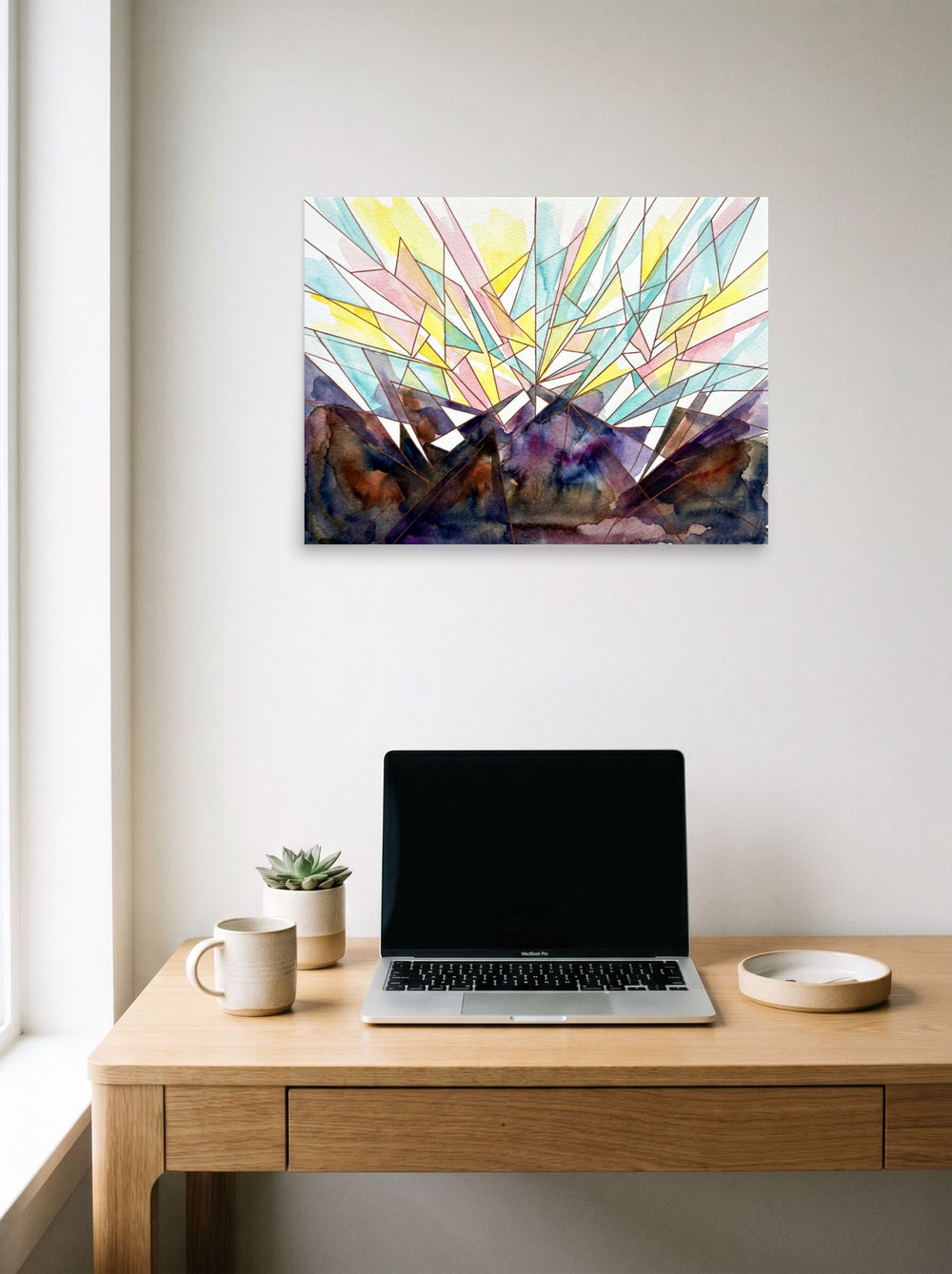 A 24x18 inch unframed paper Geometric abstract art print of 'Symphony' hanging above a worktable with a laptop.