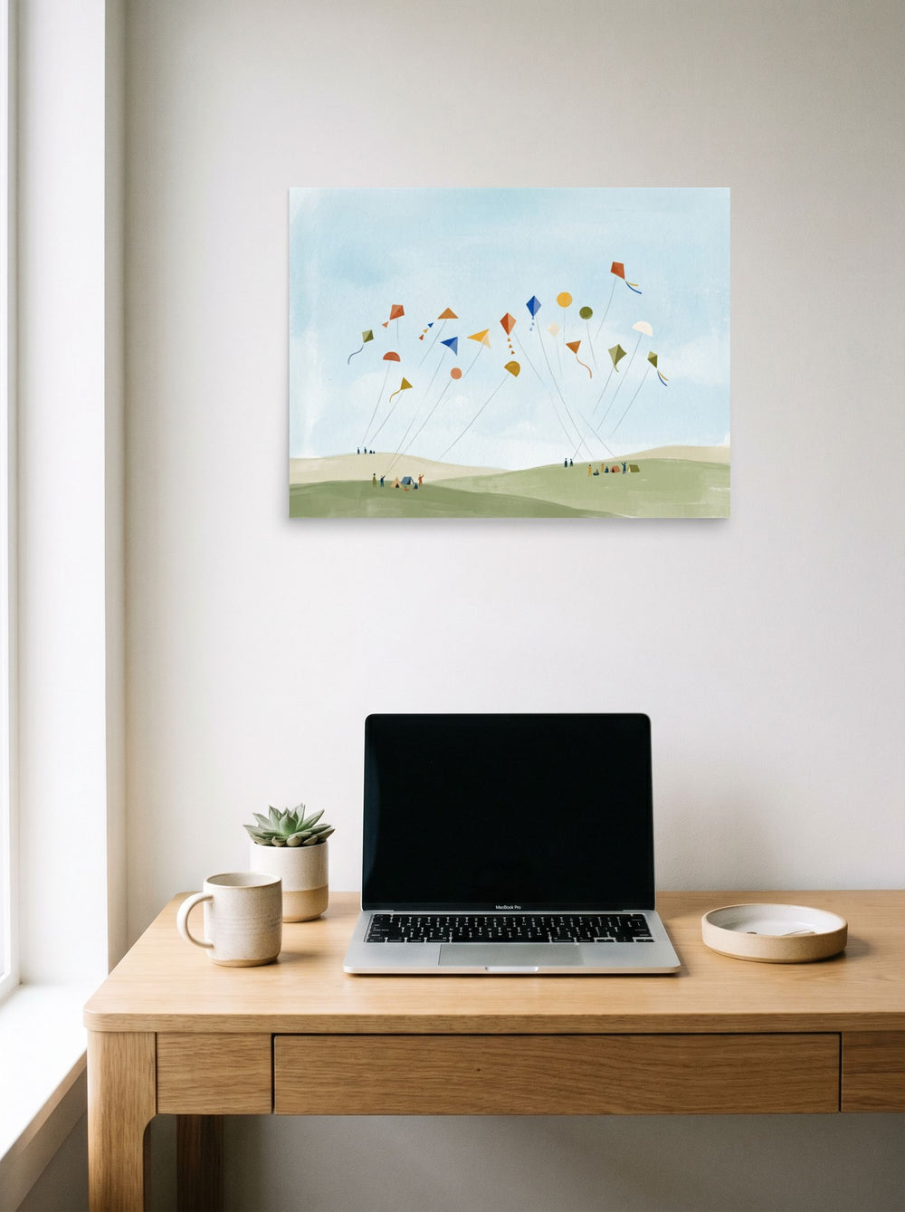 A 24x18 inch unframed paper Minimalism,Naive art print of 'Kite Festival' hanging above a worktable with a laptop.