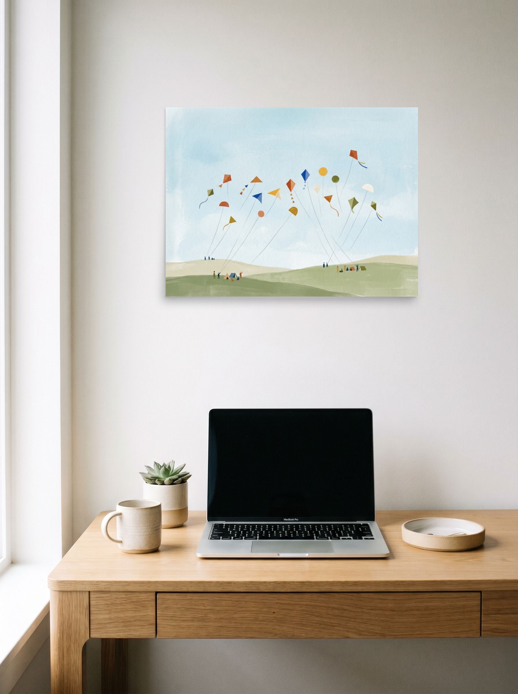 A 24x18 inch unframed paper Minimalism,Naive art print of 'Kite Festival' hanging above a worktable with a laptop.