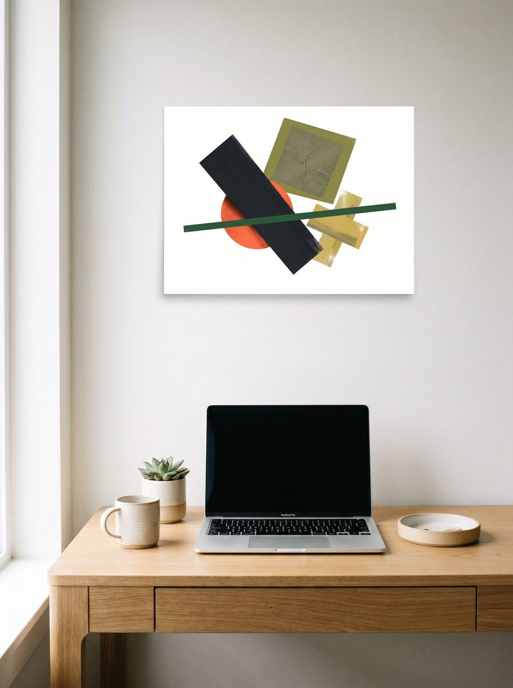 A 24x18 inch unframed paper Suprematism print of 'The Geometry of Sound' hanging above a worktable with a laptop.