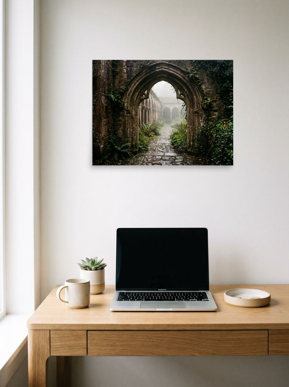 A 24x18 inch unframed paper Art photography print of 'The Forgotten Abbey' hanging above a worktable with a laptop.