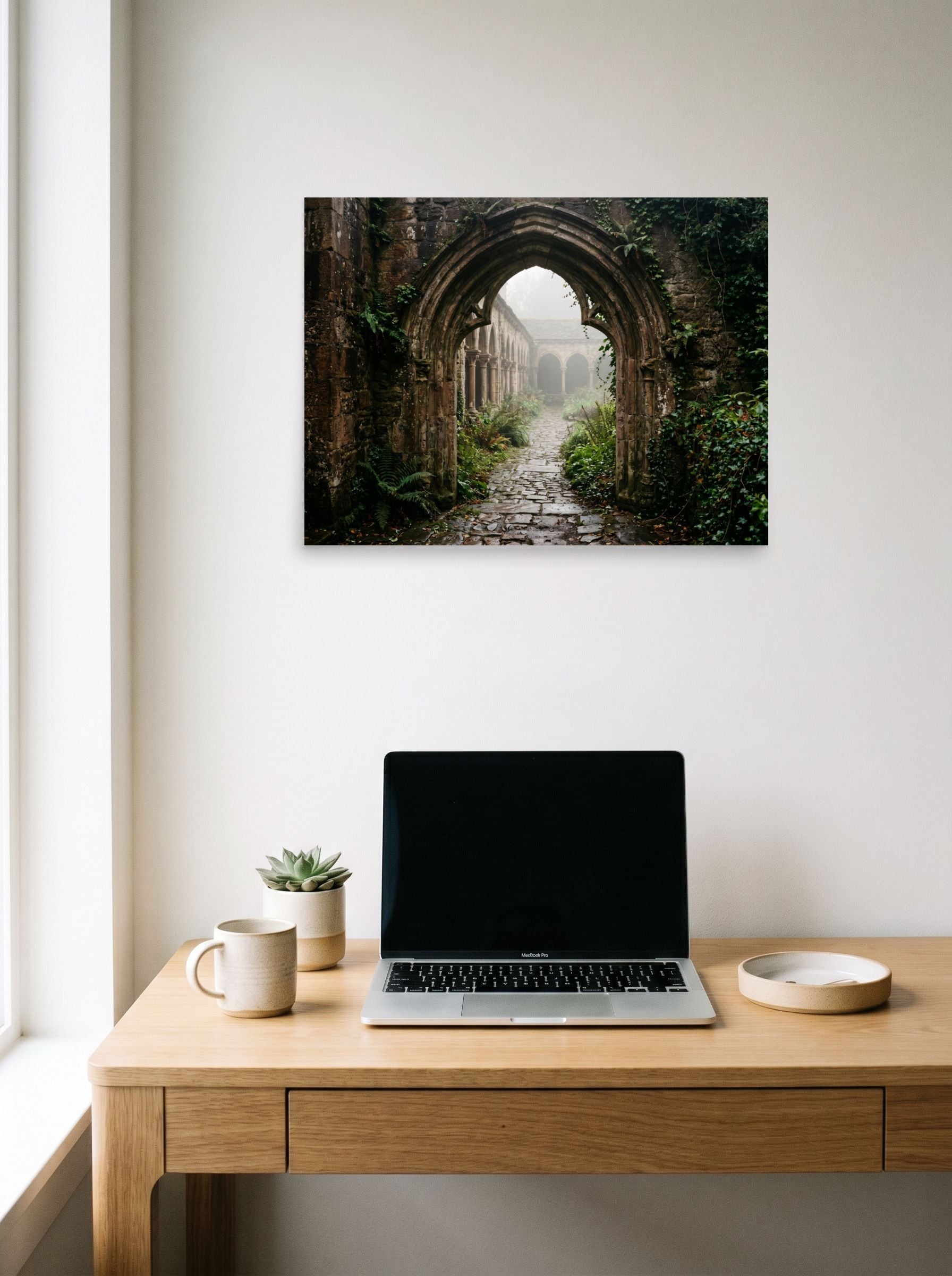 A 24x18 inch unframed paper Art photography print of 'The Forgotten Abbey' hanging above a worktable with a laptop.