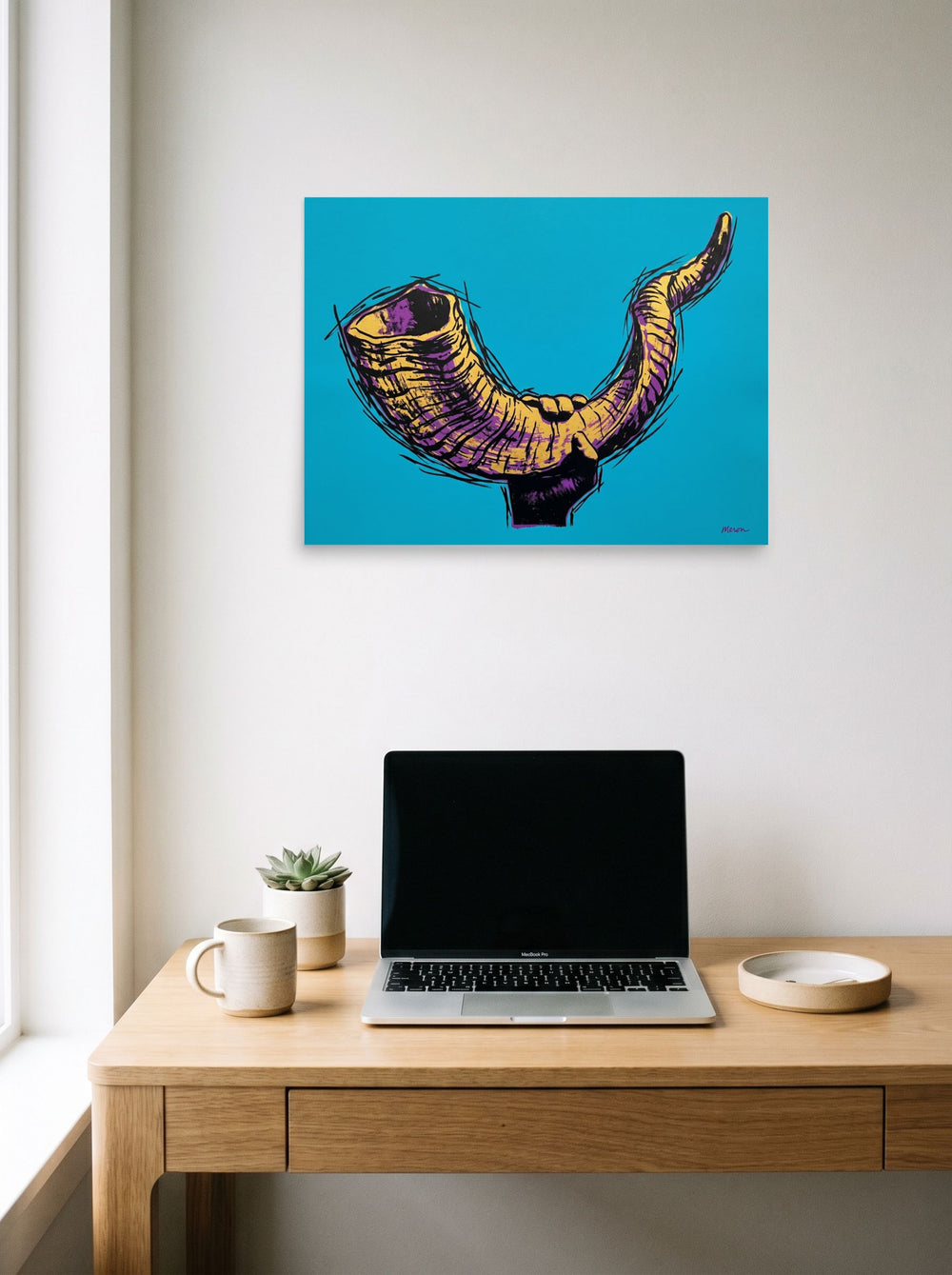 A 24x18 inch unframed paper Pop art print of 'The Golden Shofar' hanging above a worktable with a laptop.