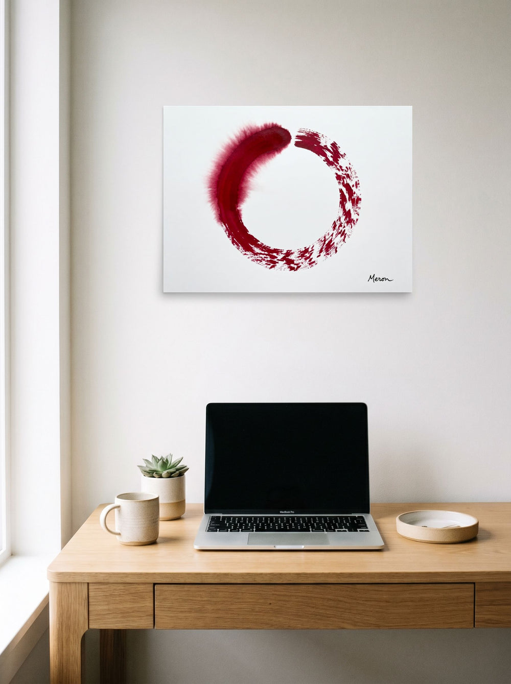 A 24x18 inch unframed paper Minimalism,Abstract expressionism print of 'Crimson Enso' hanging above a worktable with a laptop.