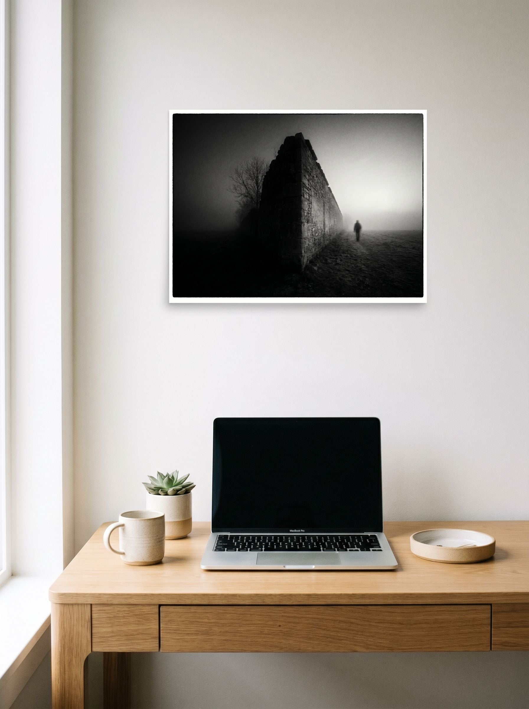 A 24x18 inch unframed paper Art photography print of 'Echoes in the Mist' hanging above a worktable with a laptop.