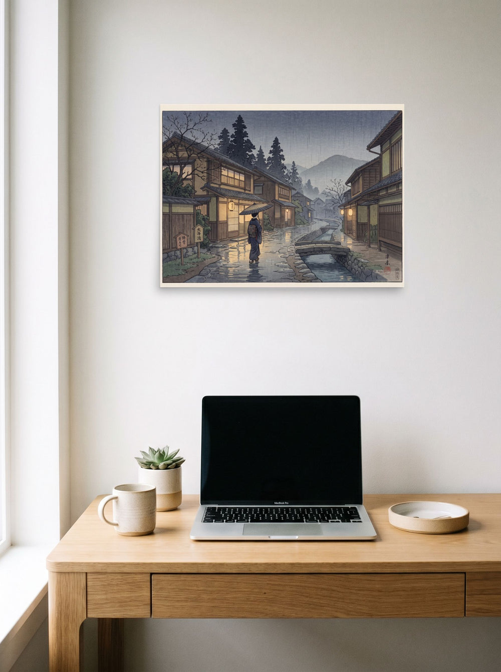 A 24x18 inch unframed paper Shin hanga print of 'Rain on Stone Street' hanging above a worktable with a laptop.