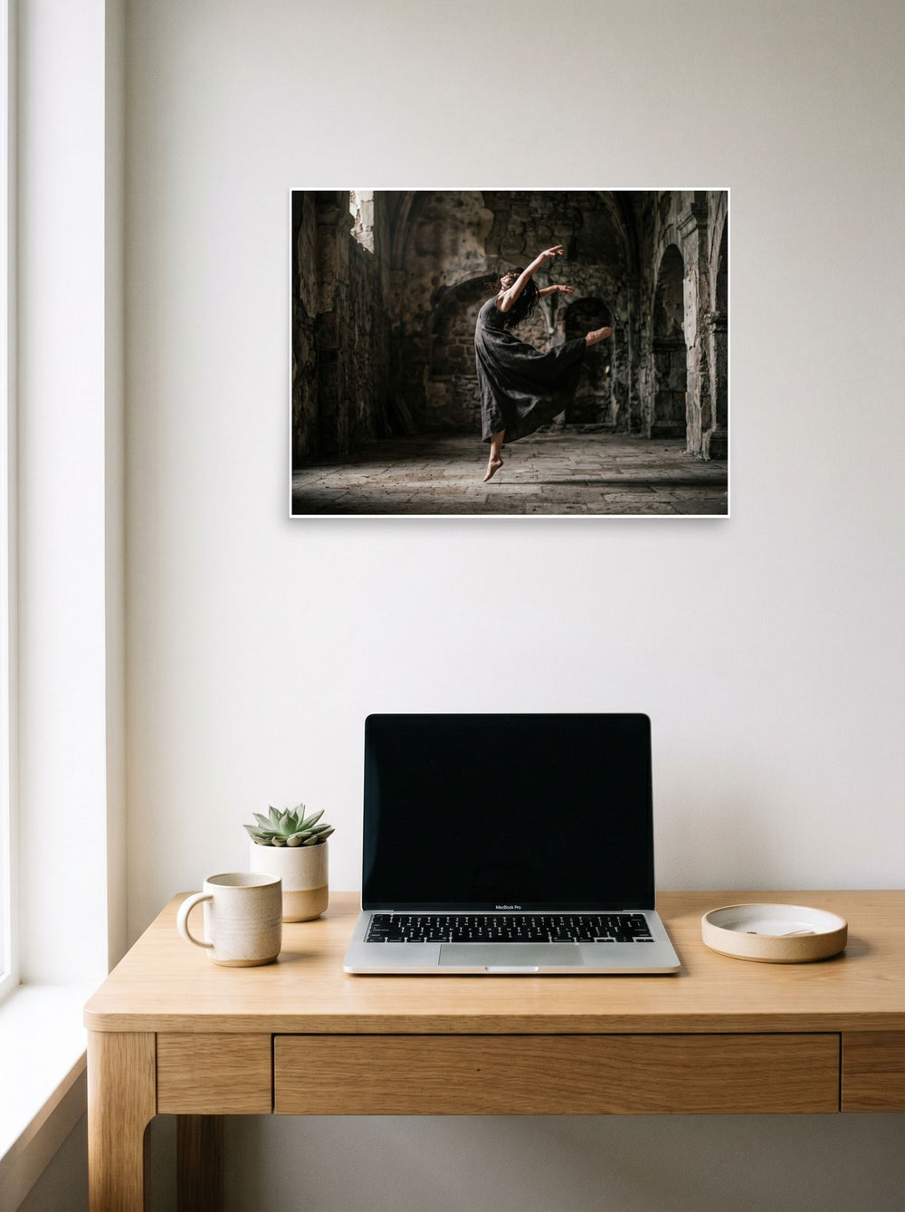 A 24x18 inch unframed paper Art photography print of 'Grace in the Ruins' hanging above a worktable with a laptop.