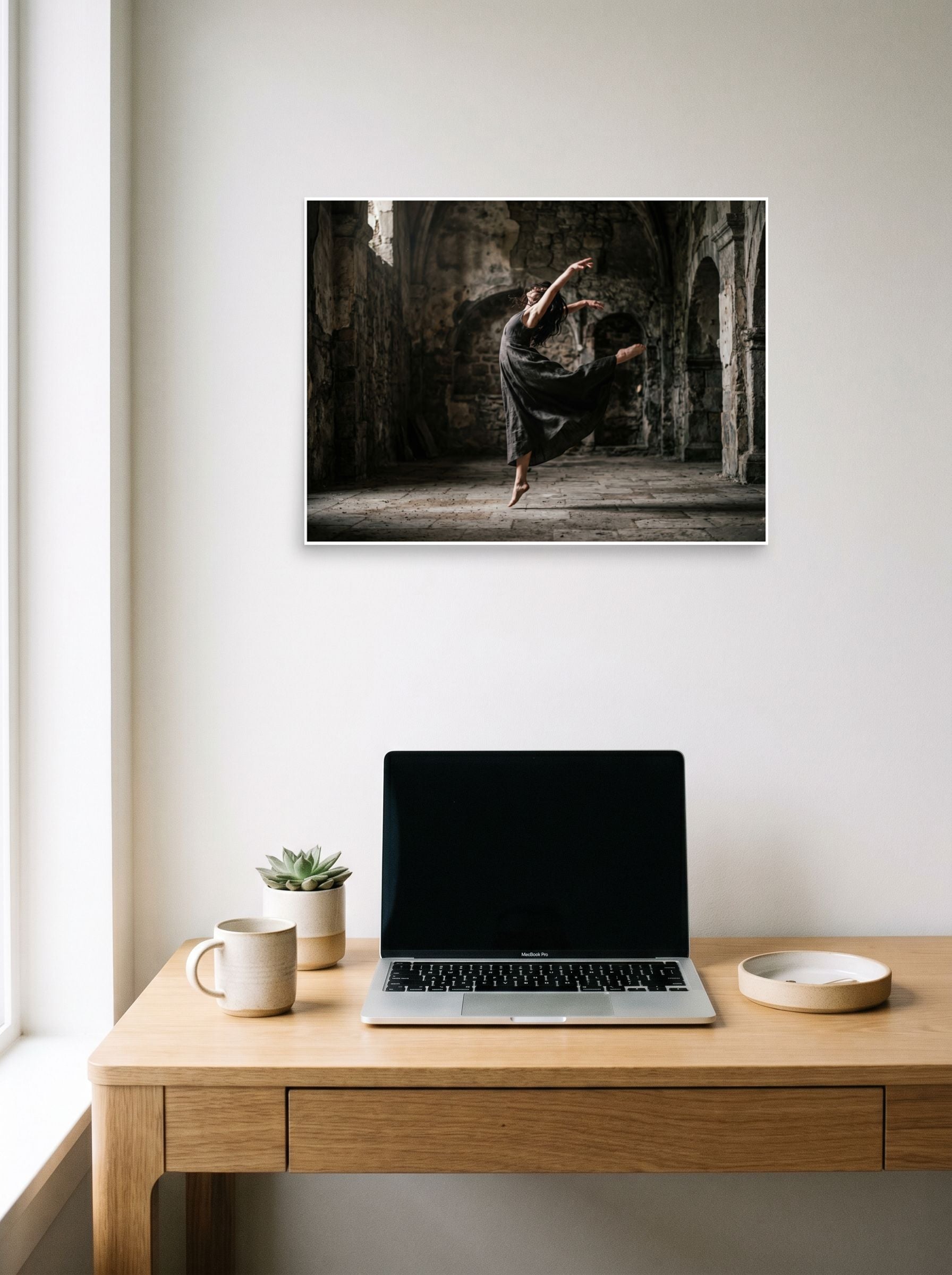 A 24x18 inch unframed paper Art photography print of 'Grace in the Ruins' hanging above a worktable with a laptop.