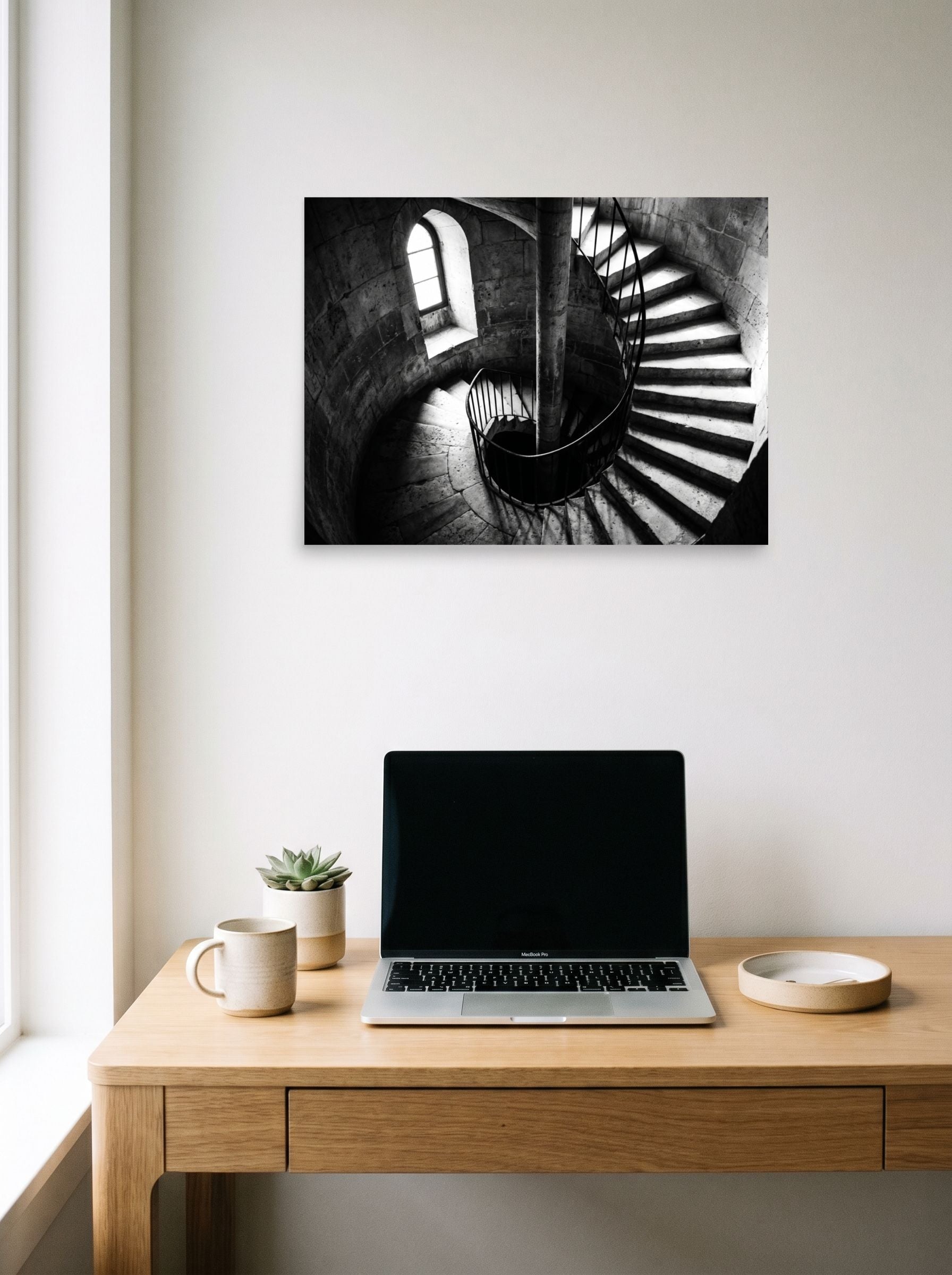 A 24x18 inch unframed paper Art photography print of 'Descent into Light' hanging above a worktable with a laptop.