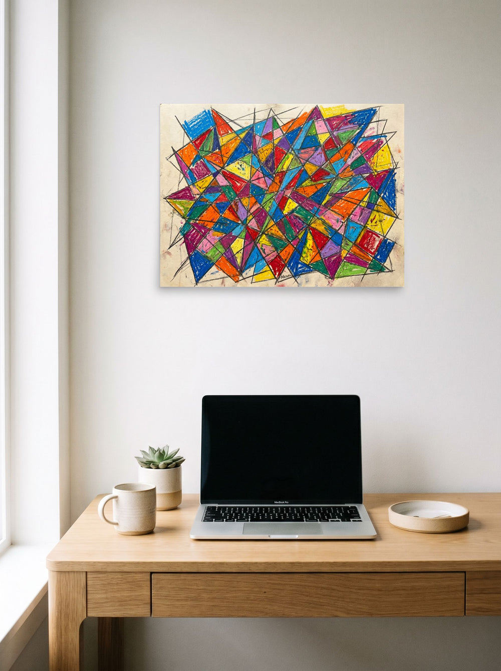 A 24x18 inch unframed paper Geometric abstract art,Cubism print of 'Prismatic Chaos' hanging above a worktable with a laptop.