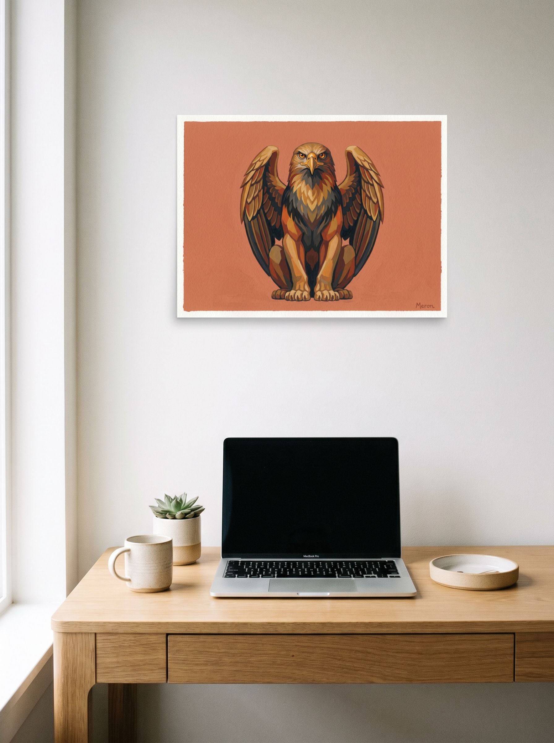 A 24x18 inch unframed paper Art Deco print of 'The Golden Griffin' hanging above a worktable with a laptop.