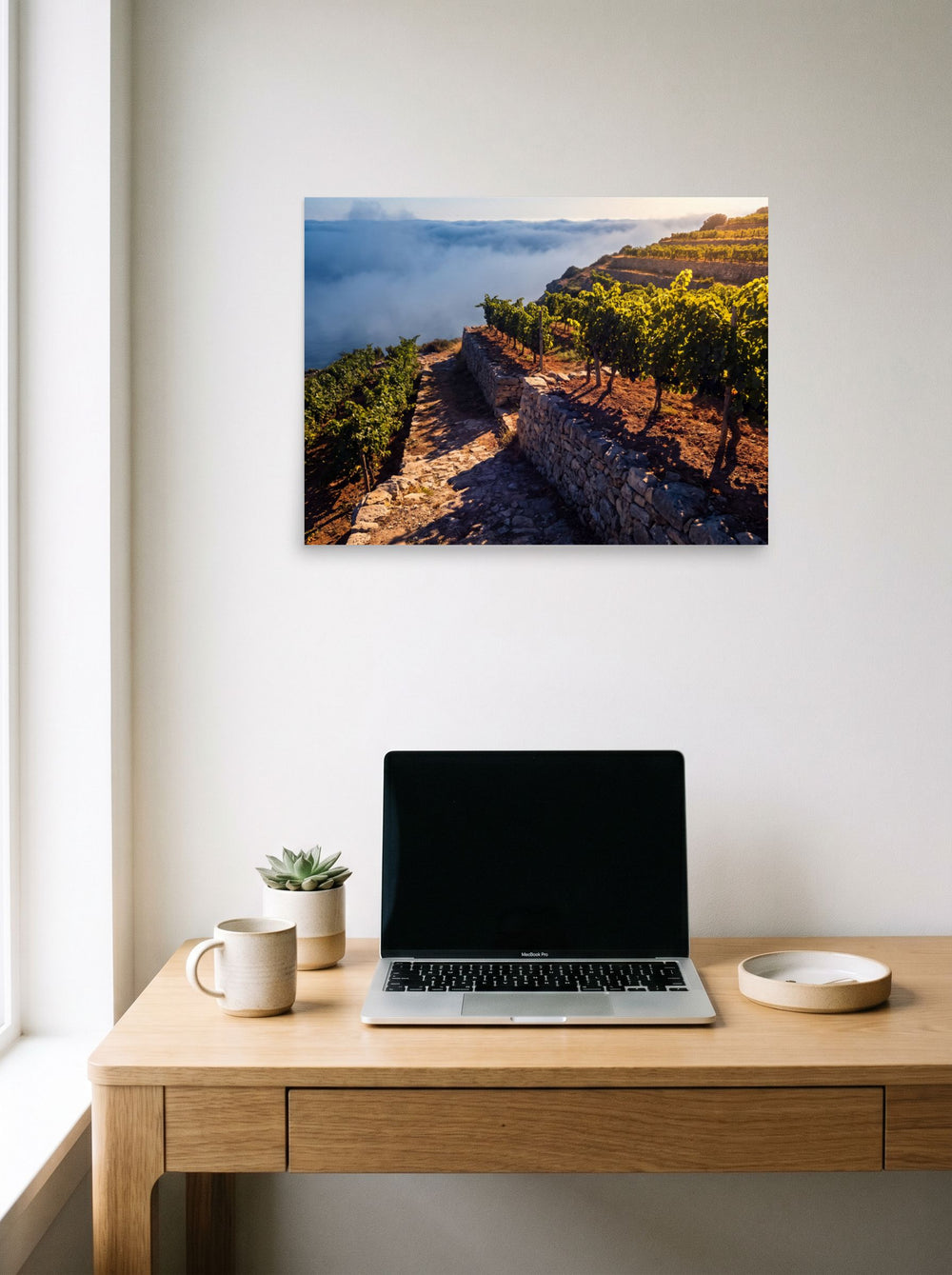 A 24x18 inch unframed paper Art photography print of 'Vineyard Above the Clouds' hanging above a worktable with a laptop.