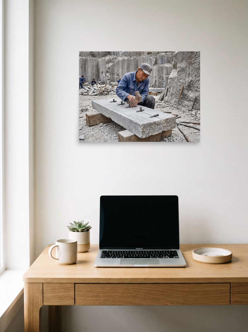 A 24x18 inch unframed paper version of 'Splitting the Stone', Art photography wall art, hanging above a worktable with a laptop.