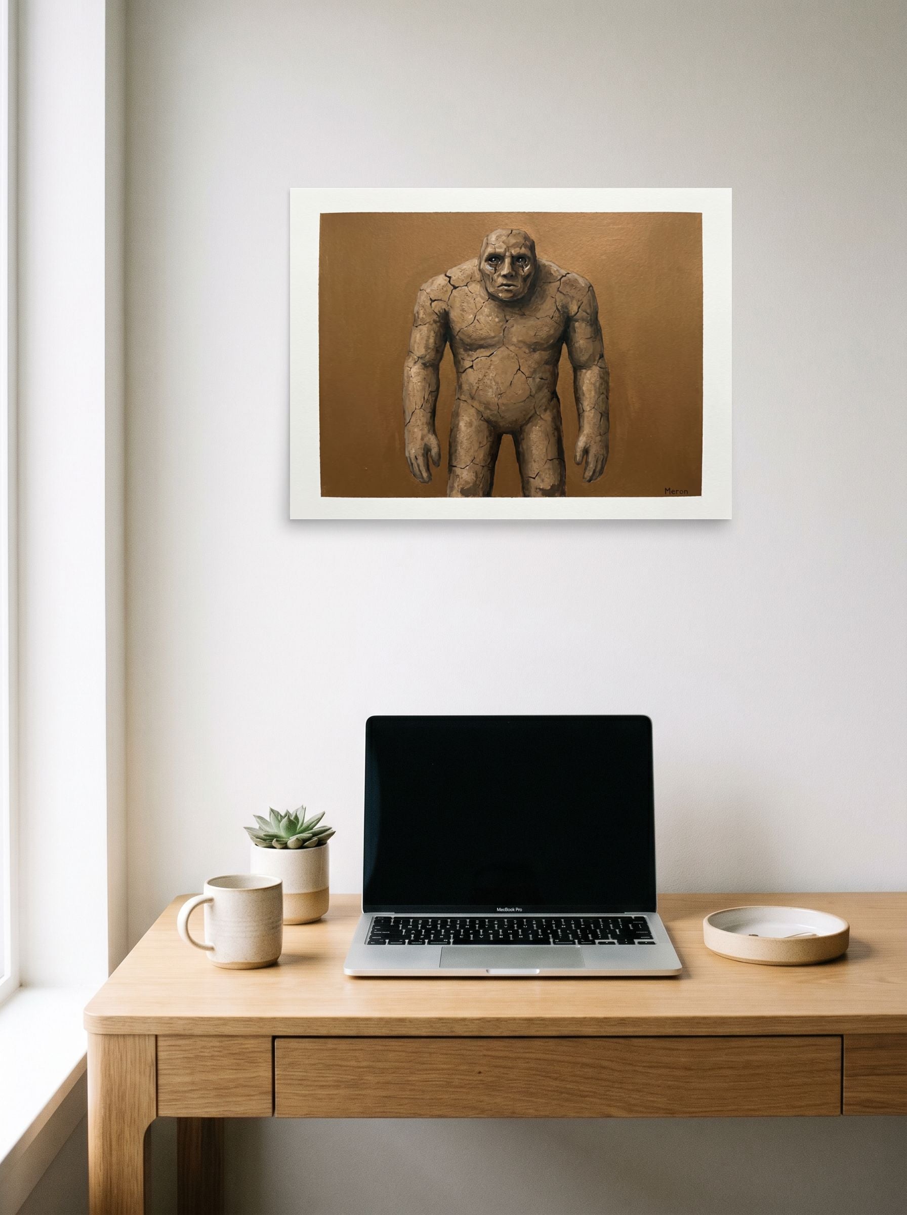 A 24x18 inch unframed paper Surrealism,Figurative art print of 'The Weeping Golem' hanging above a worktable with a laptop.