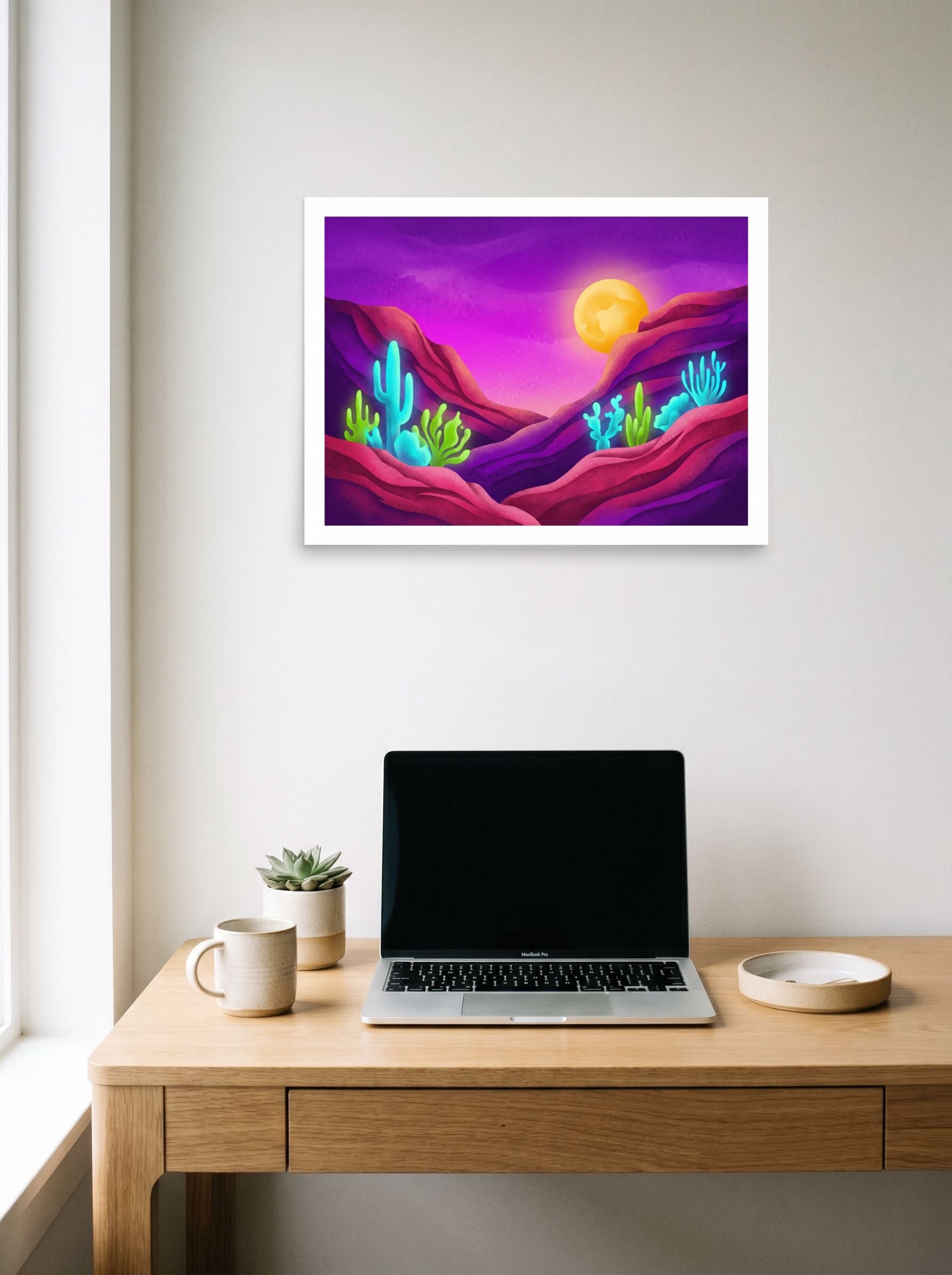 A 24x18 inch unframed paper Surrealism,Psychedelic art print of 'Bioluminescent Desert' hanging above a worktable with a laptop.
