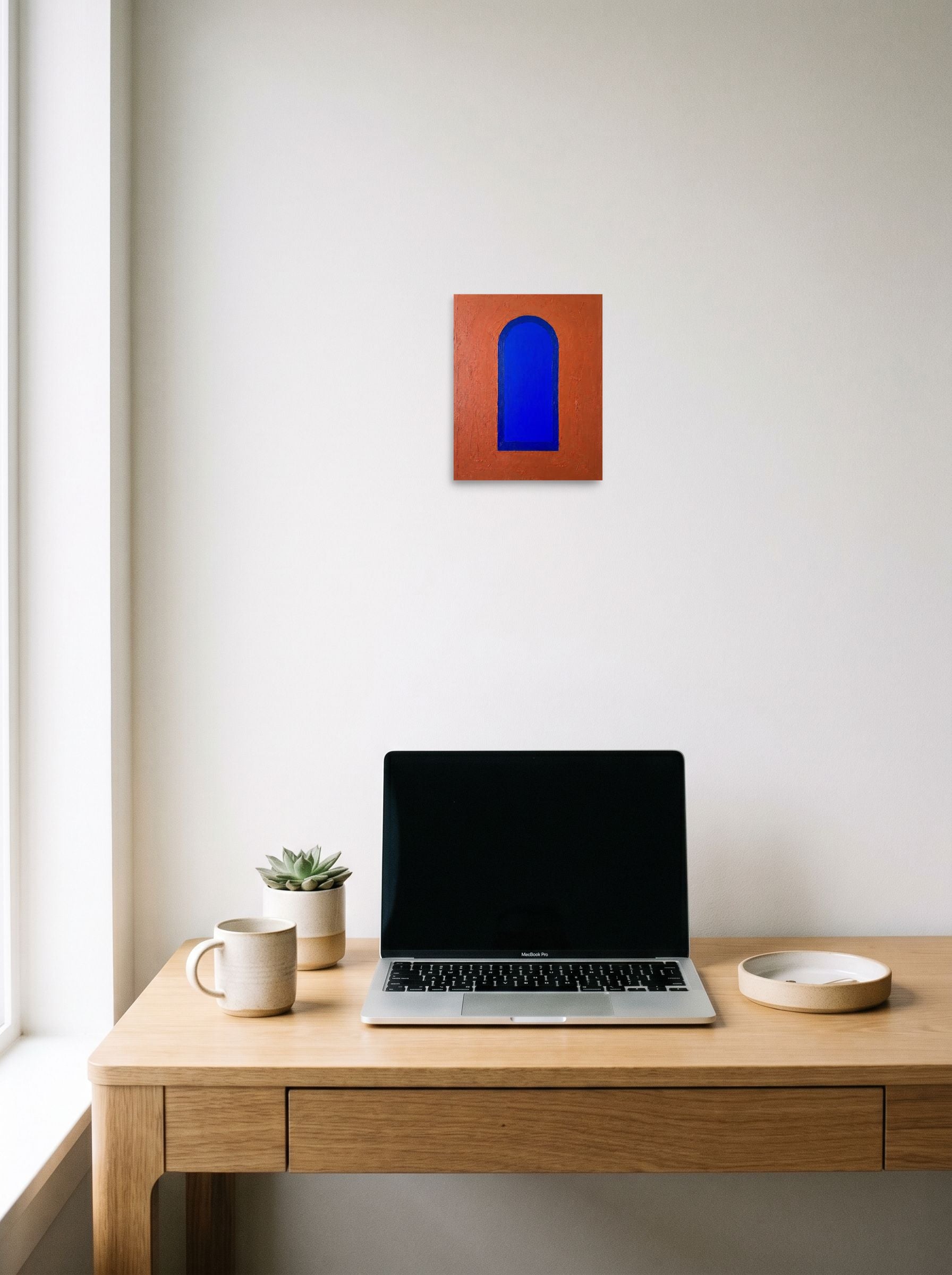 A 8x10 inch unframed paper Minimalism print of 'The Blue Arch' hanging above a worktable with a laptop.