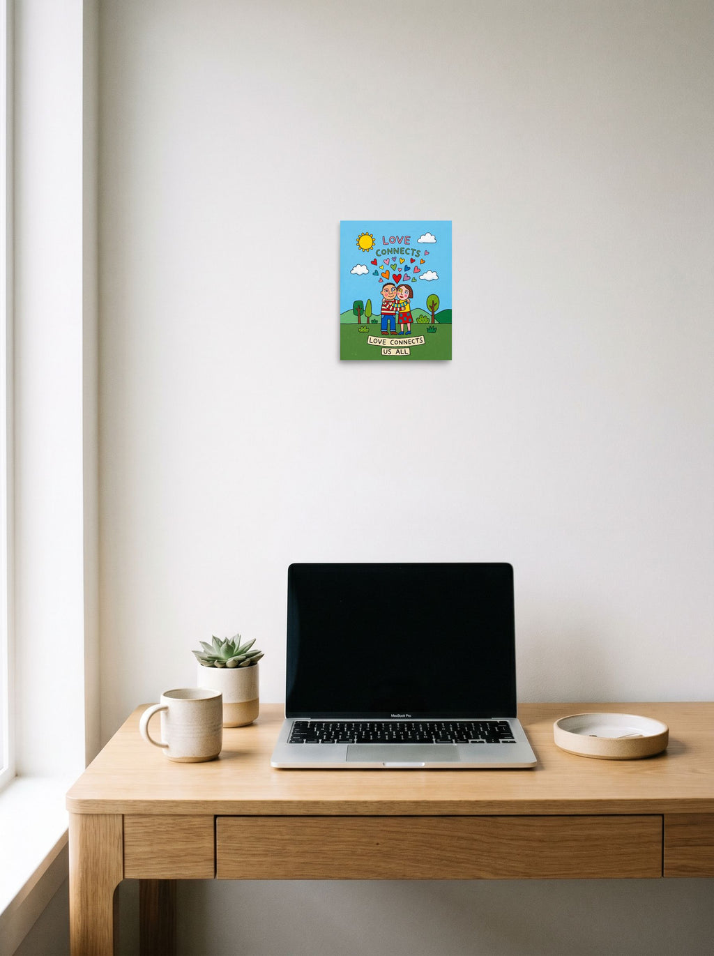 A 8x10 inch unframed paper Naive art print of 'Love Connects Us All' hanging above a worktable with a laptop.