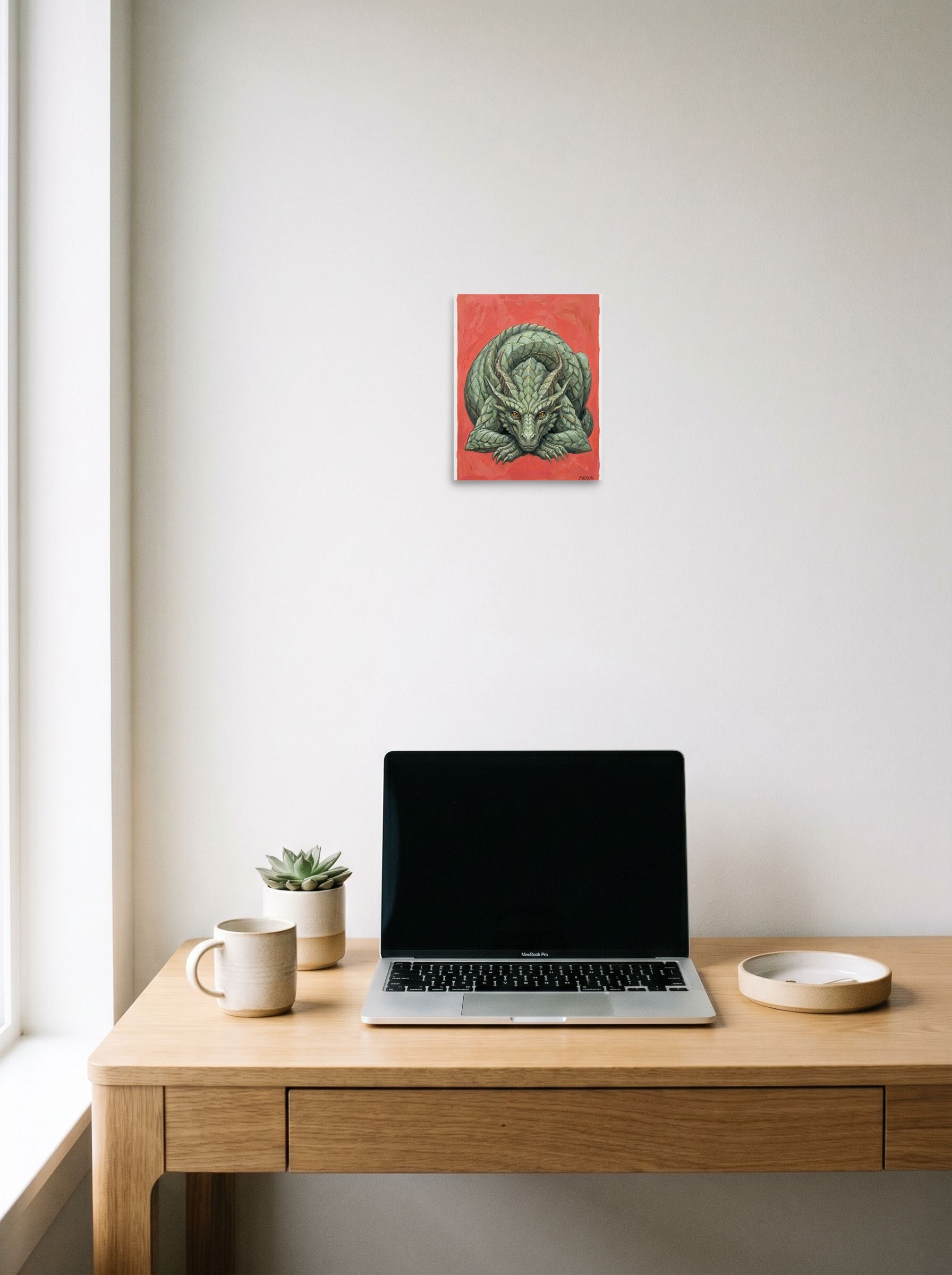 A 8x10 inch unframed paper Fantastic realism print of 'Slumbering Drake' hanging above a worktable with a laptop.