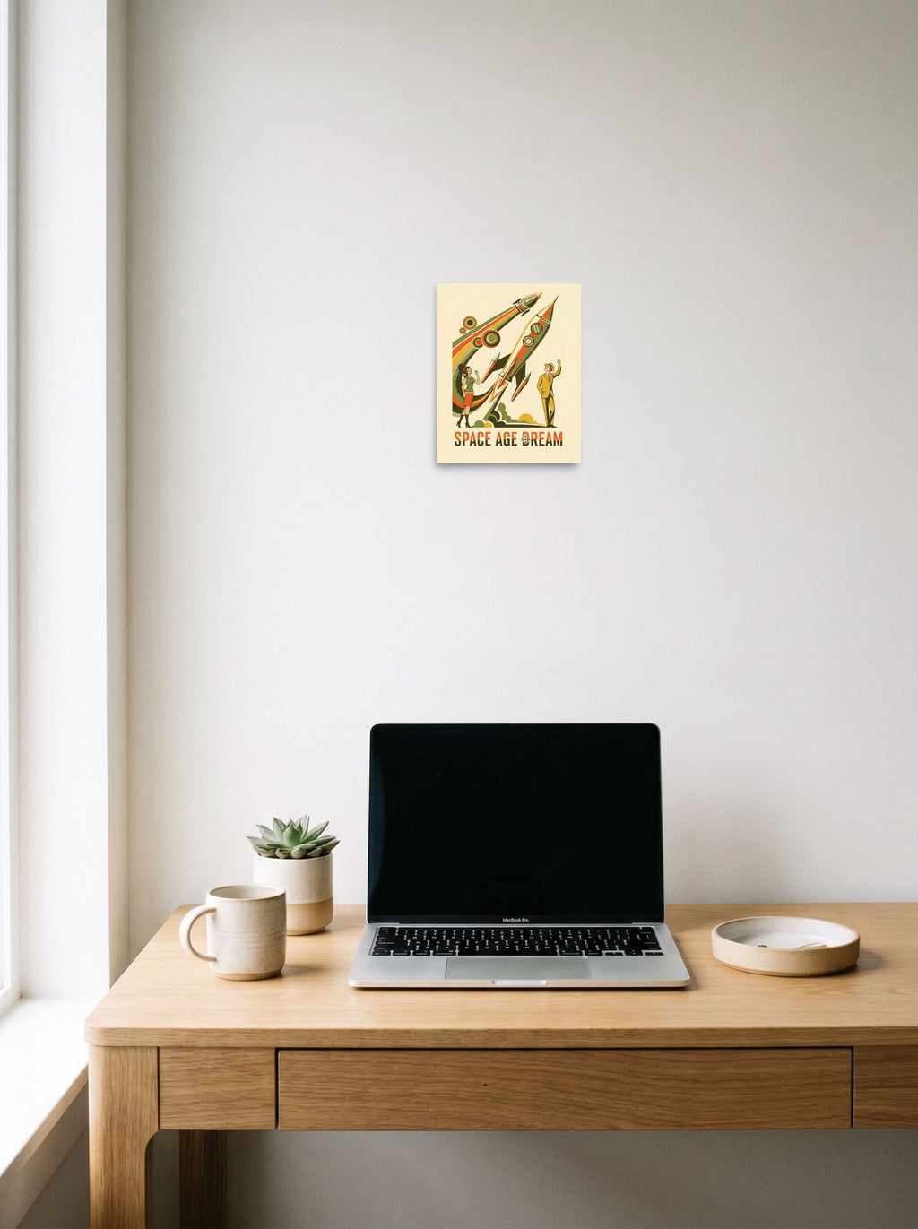 A 8x10 inch unframed paper Retrofuturism,Pop art print of 'Space Age Dream' hanging above a worktable with a laptop.