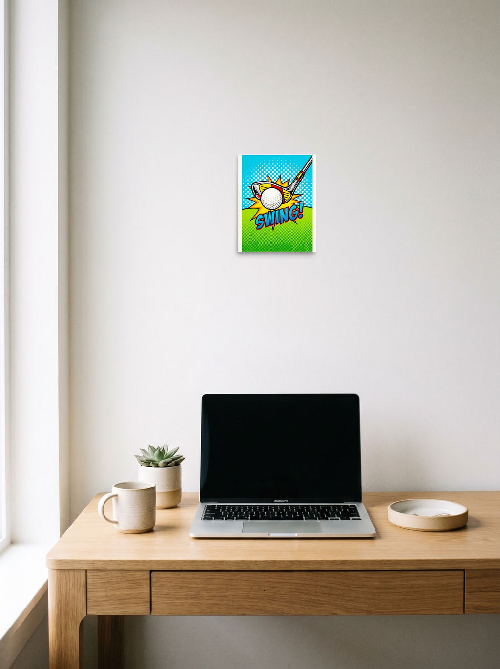 A 8x10 inch unframed paper Pop art print of 'Comic Swing' hanging above a worktable with a laptop.