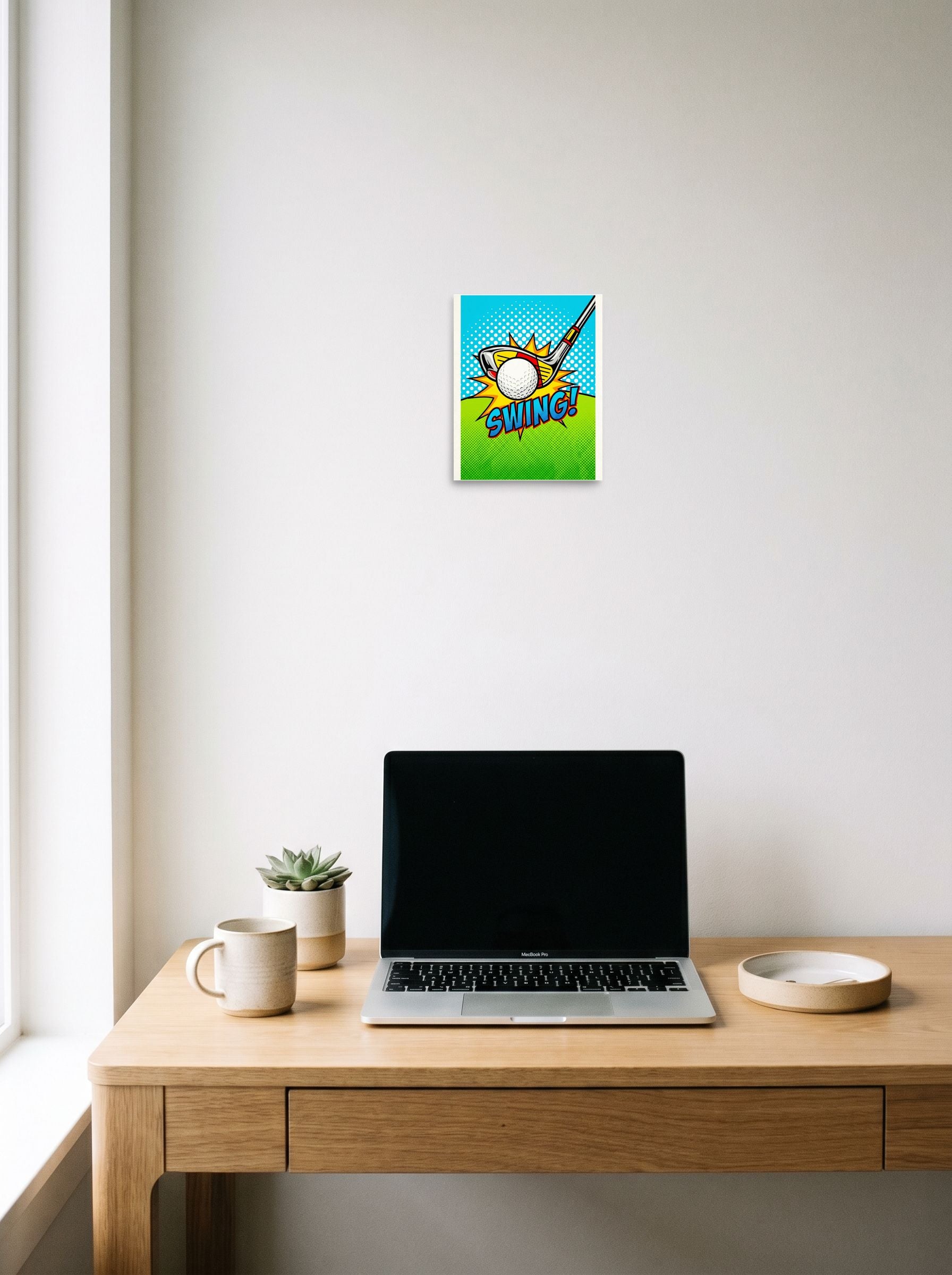 A 8x10 inch unframed paper Pop art print of 'Comic Swing' hanging above a worktable with a laptop.