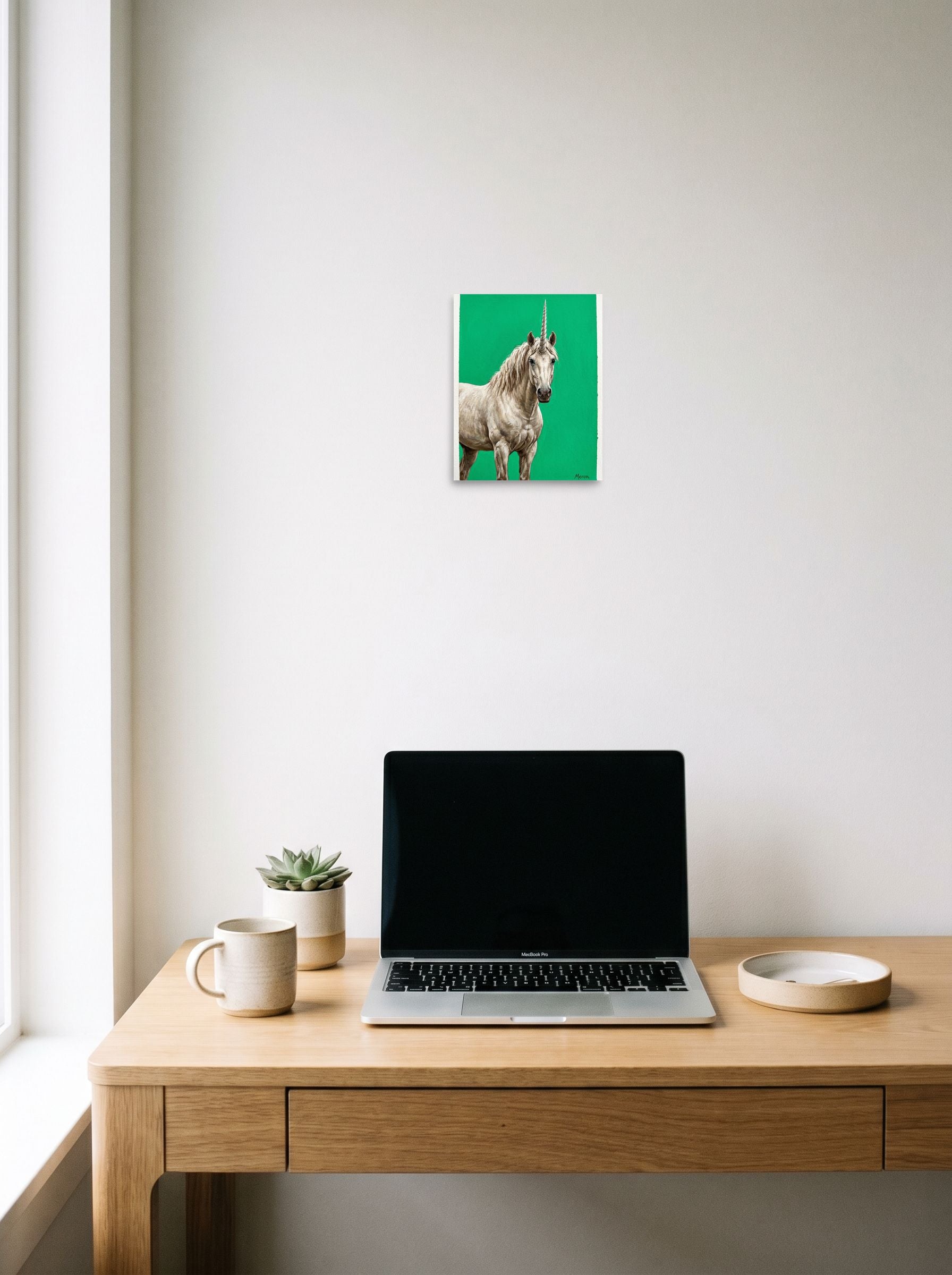 A 8x10 inch unframed paper Realism print of 'The Emerald Unicorn' hanging above a worktable with a laptop.